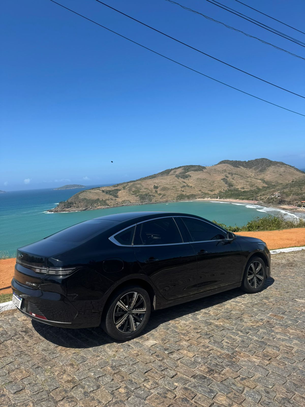 Carro Sedan executivo estacionado em um mirante com vista para uma praia em Angra dos Reis